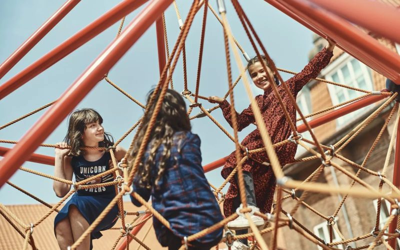 Tre piger leger på et klatrestativ.