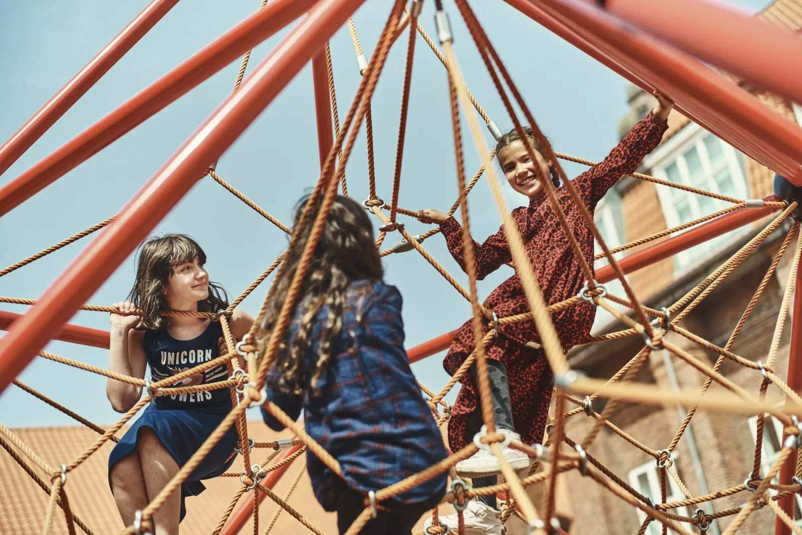 Tre piger leger på et klatrestativ.