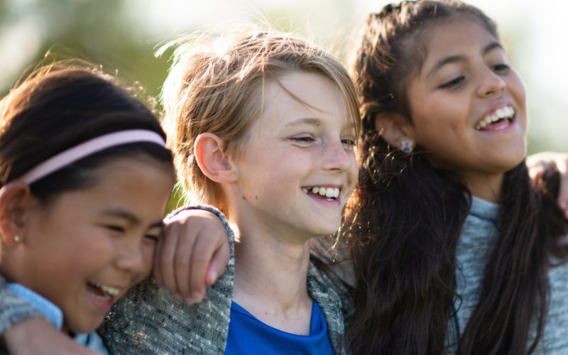 Tre børn holder hinanden om skuldrene og griner