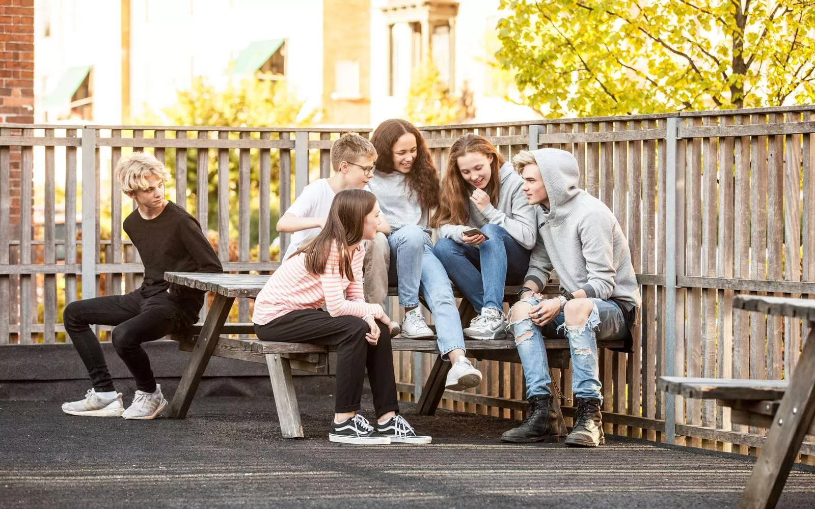 Fire børn sidder på en bænk i en gruppe, med en enkelt dreng der sidder for sig selv