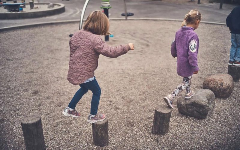 To piger går på stammer og sten lagt ud på en legeplads