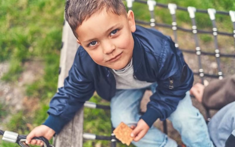 Dreng sidder på en gynge med en kiks i hånden og kigger op på kameraet