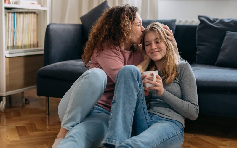 Kvinde sidder på gulvet og kysser hovedet på pige