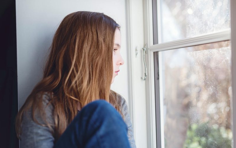 Pige sidder i vindueskarm og kigger ud af vindue