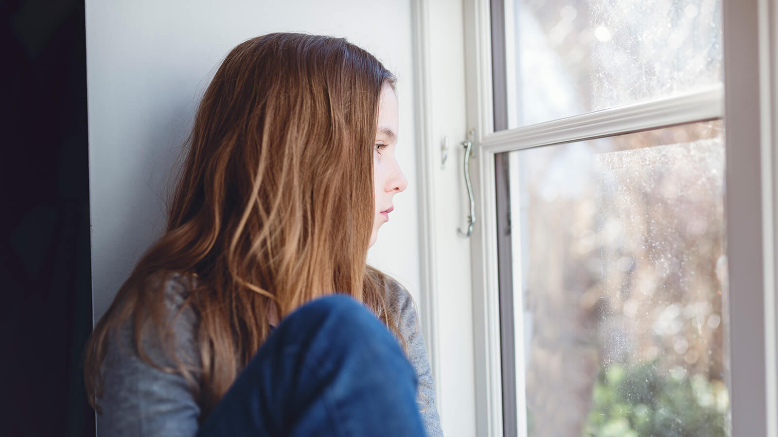 Pige sidder i vindueskarm og kigger ud af vindue